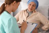 Nurse holding clipboard and writing next to cancer patient who is lying in bed