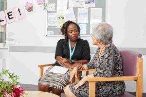 An Admiral Nurse speaking with a service user. They are both sat on chairs in a room having a conversation.